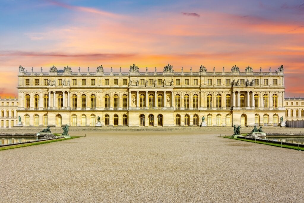 Vista da arte da frente do Palácio de Versalhes no fim da tarde com céu azul e rosa