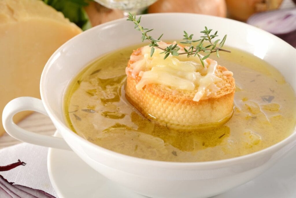 Sopa de cebola em um recipiente de porcelana branca com pão tostado com queijo derretido em cima 