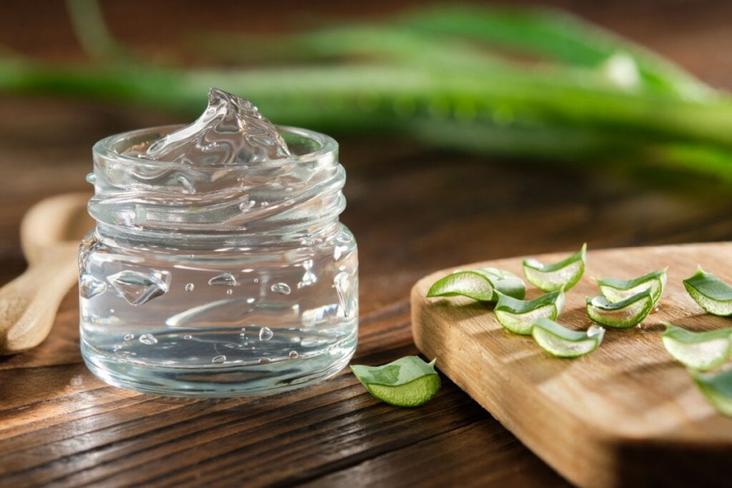 Pote transparente com gel de babosa ao lado de pedaços picados da planta