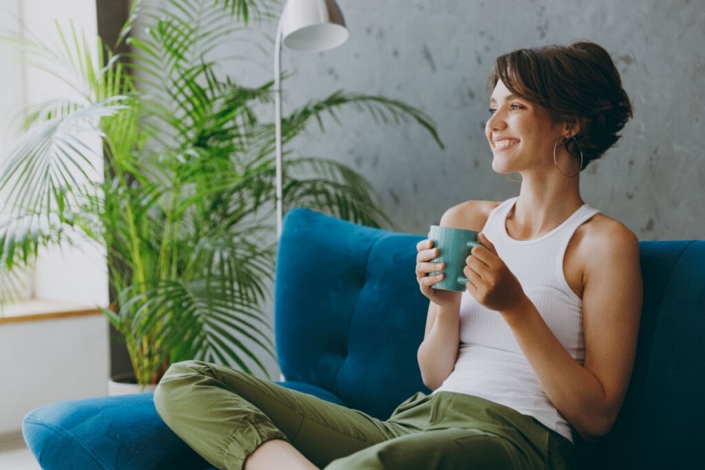 Mulher tomando chá, sentada no sofá, com uma expressão sorridente