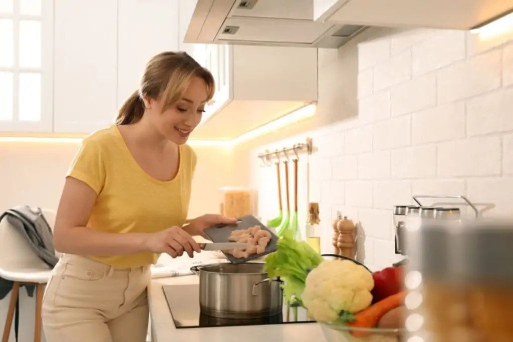 Mulher sorrindo cozinhando frango em cozinha