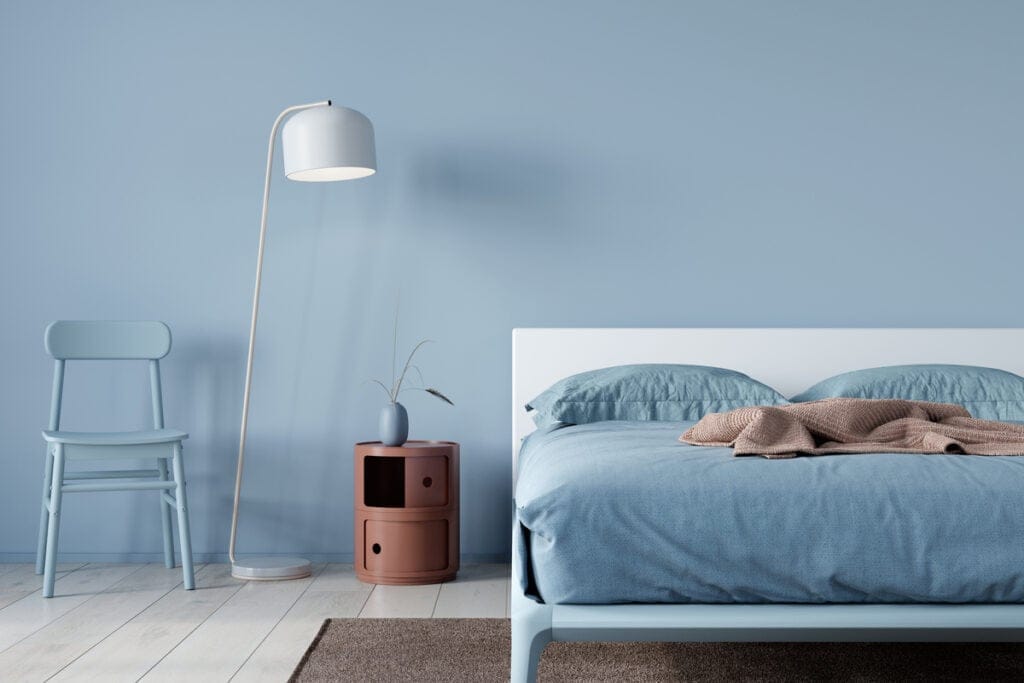 Quarto com parede azul, abajur e cama com lençol azul