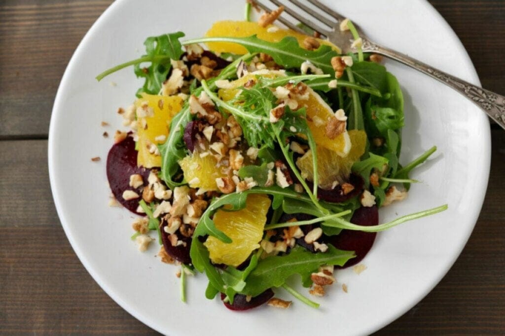 Salada de rúcula com beterraba, laranja e nozes em um prato branco 