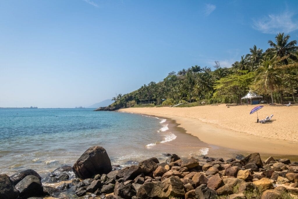 Praia da Feiticeira, em Ilhabela, com suas águas cercadas por pedras e coqueiros