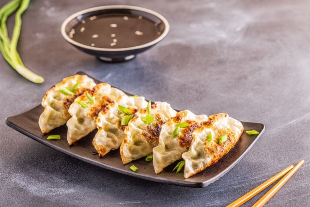 Recipiente marrom com gyozas polvilhadas com cebolinha
