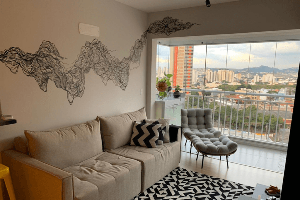 Sala de estar com uma parede branca com pintura em preto, sofá bege, tapete e varanda na lateral