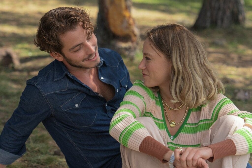 Homem e mulher sentados em um parque em cena da série "Próximo" 
