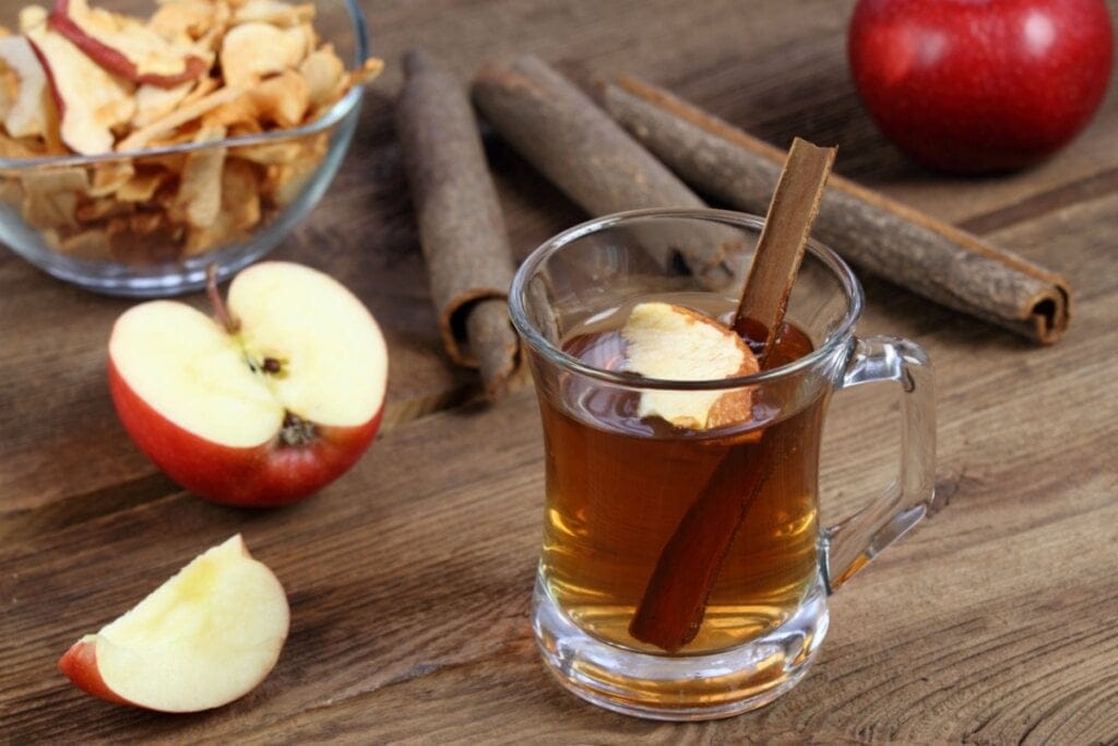 Xícara de vidro com chá de canela e maçã em cima de uma mesa de madeira