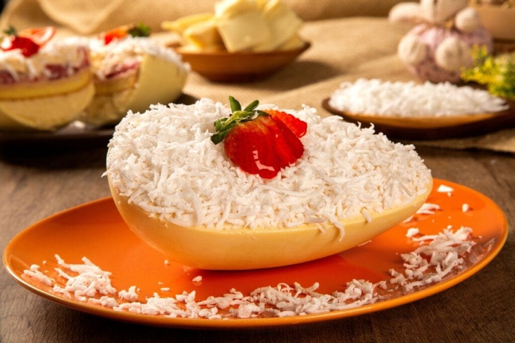 Ovo de Páscoa de chocolate branco recheado com beijinho, e com coco ralado por cima com morango em prato de cerâmica laranja em cima de mesa de madeira