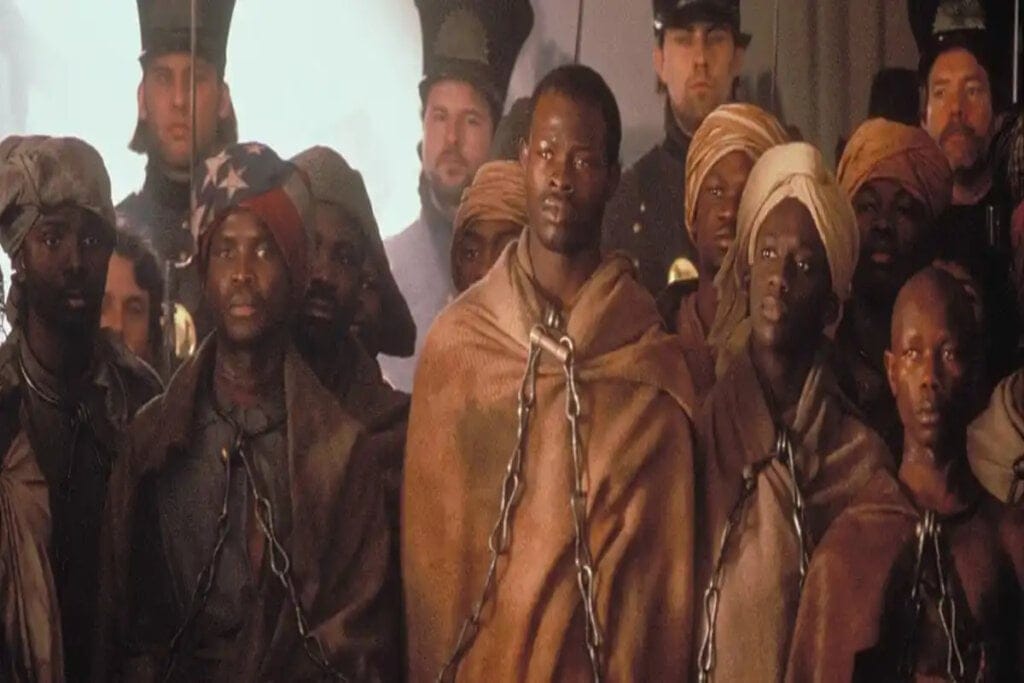 imagem com homens negros com roupas marrom e acorrentados pelo pescoço