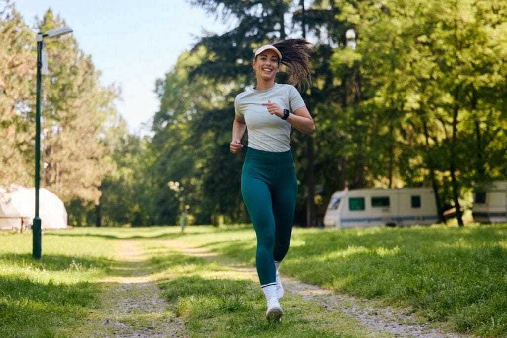 Mulher usando roupas de academia, uma camiseta cinza, uma calça verde e uma viseira correndo ao ar livre
