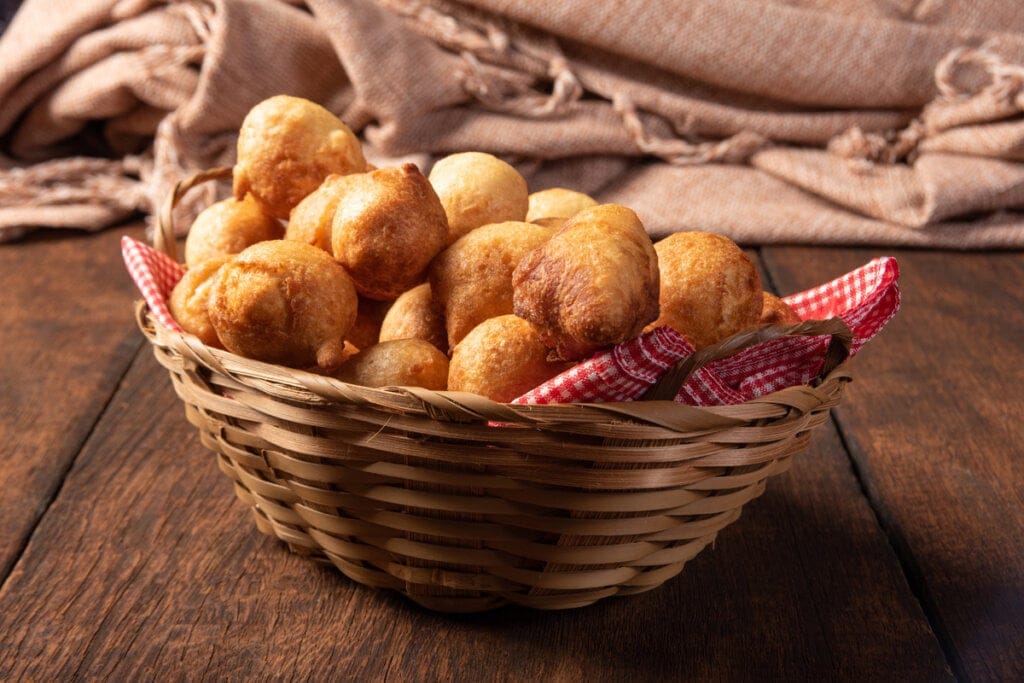 Bolinho de chuva de fubá em uma cesta de palha com pano quadriculado vermelho e branco 