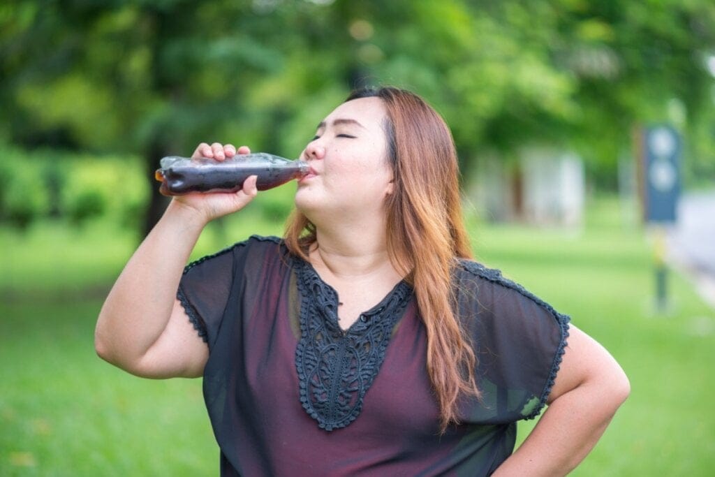 Mulher com sobrepeso tomando refrigerante diretamente da garrafa em um ambiente ao ar livre