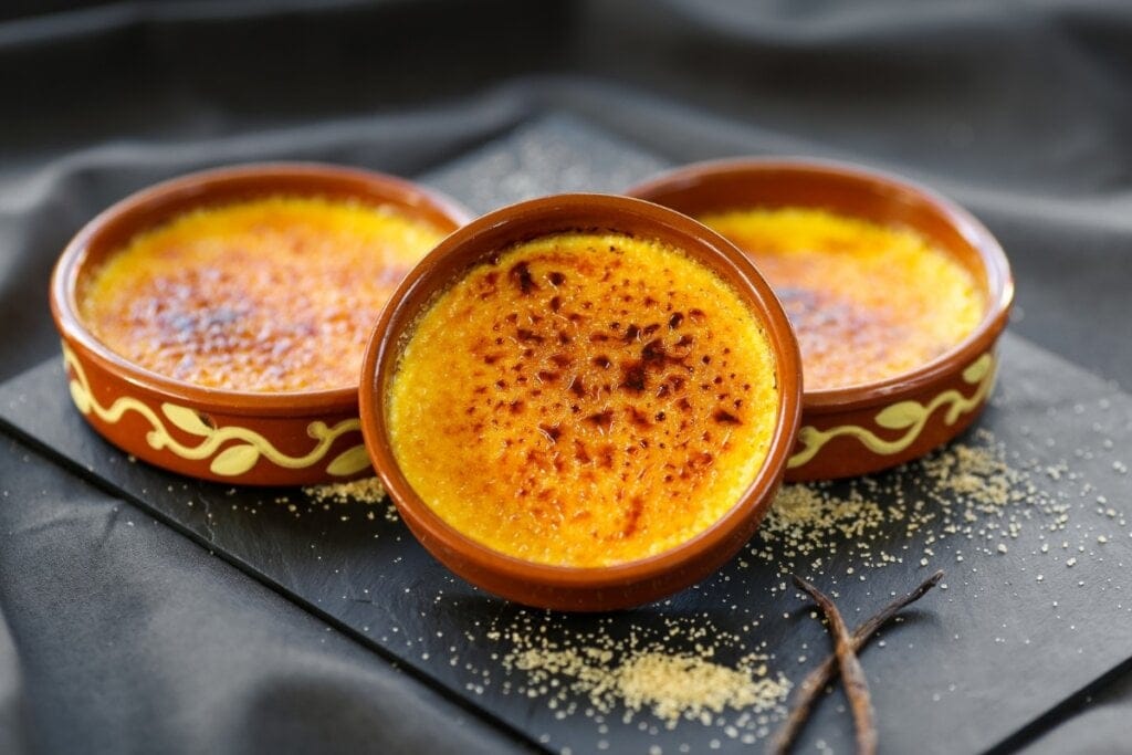três recipientes marrons com brûlée em cima de superfície preta polvilhada com açúcar