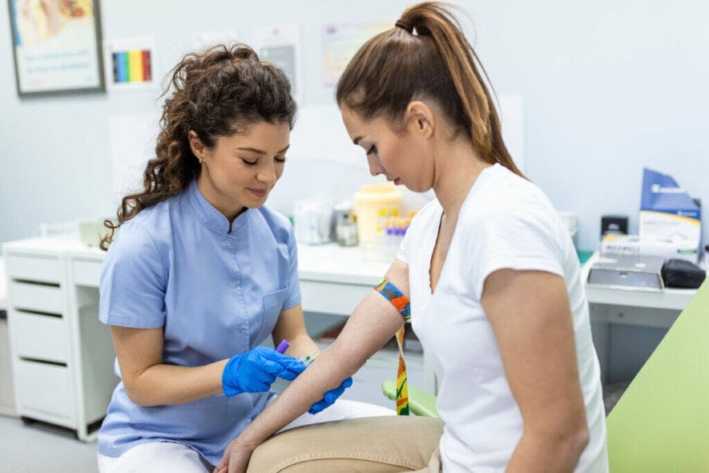 Médica coletando sangue de uma mulher. Ambas sentadas