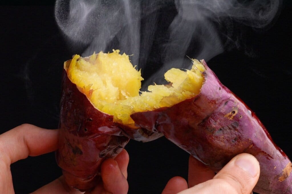 Uma batata-doce partida ao meio com fumaça saindo em fundo escuro