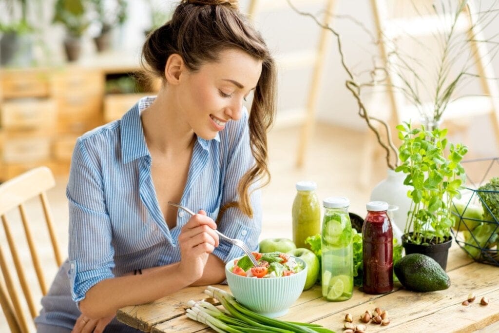 Mulher sentada e  comendo salada em um recipiente branco
