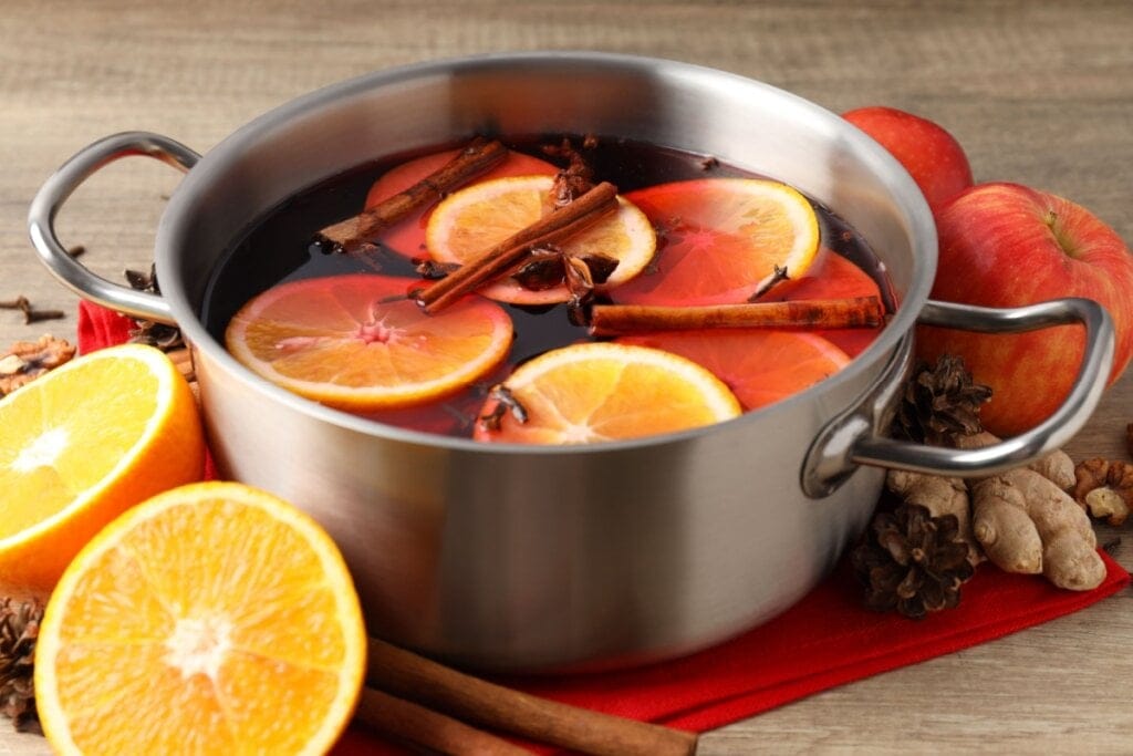 Panela de metal com vinho quente, rodelas de laranja, canela em pau e anis-estrelado em cima de um pano vermelho 