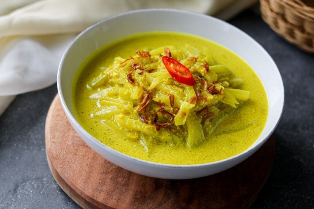 Recipiente branco com curry de chuchu, cebola frita e pimenta dedo-de-moça em cima.