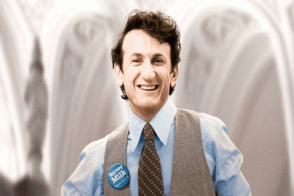 Imagem de um homem com cabelo curto, usando uma camisa social azul, uma grava marrom listrada e um colete cinza sorrindo