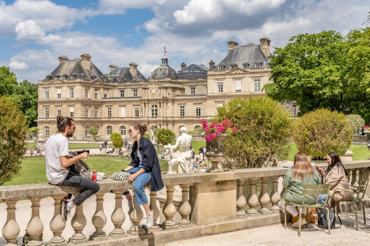 Casais aproveitando o dia ensolarado nos Jardins de Luxemburgo em Paris, com palácio ao fundo