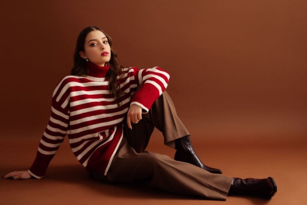 Mulher com suéter listrado vermelho e branco, calça marrom e botas escuras posando
