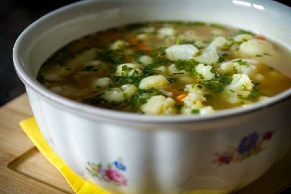 Recipiente branco com sopa de couve-flor com cenoura, cebolinha e salsa