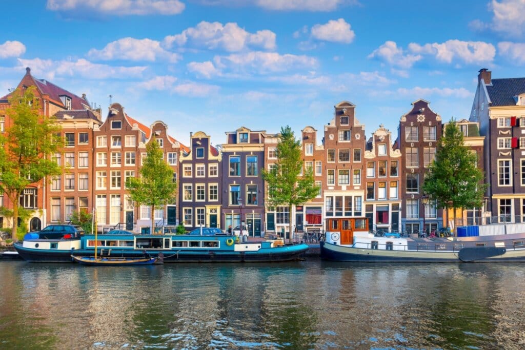 Imagem de um rio com prédios de tijolos ao fundo em Amsterdã