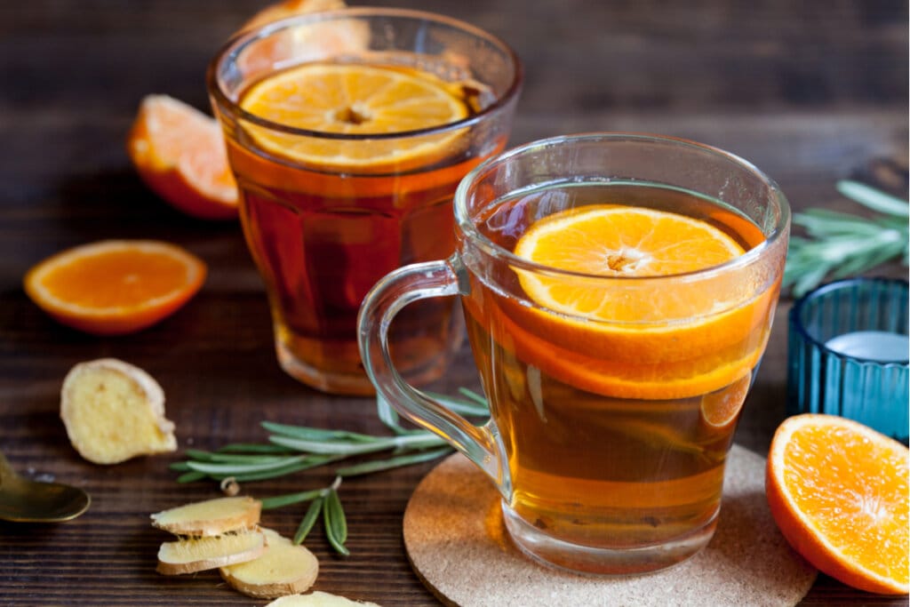 Xícara de vidro transparente com chá e rodelas de laranja em cima de uma mesa de madeira