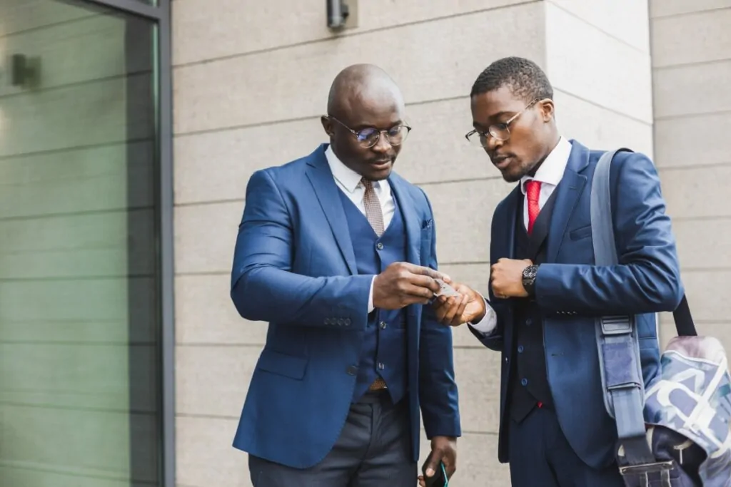 Dois profissionais de terno trocando cartões de visita em um ambiente corporativo ao ar livre