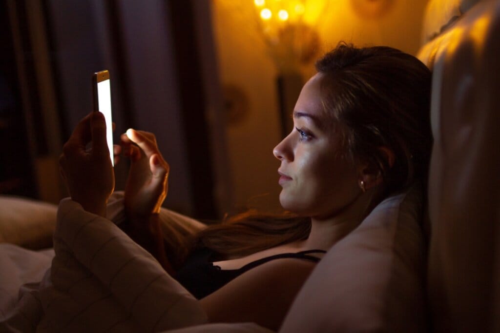 Jovem usando o celular deitada na cama antes de dormir