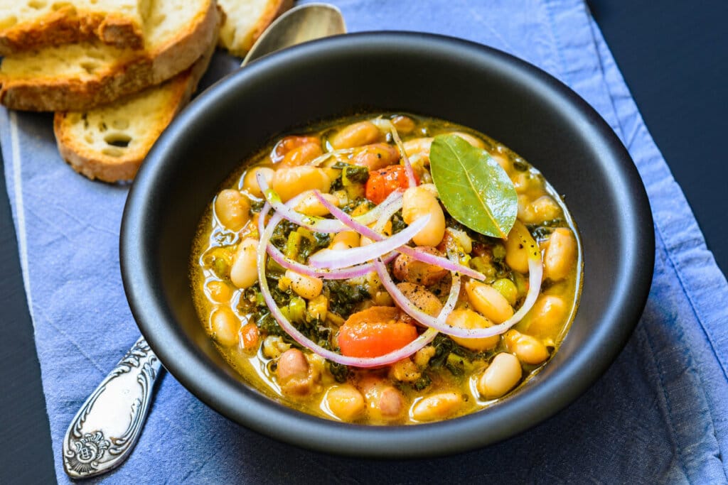 Recipiente preto com sopa de feijão com cebola, folha de louro e cenoura