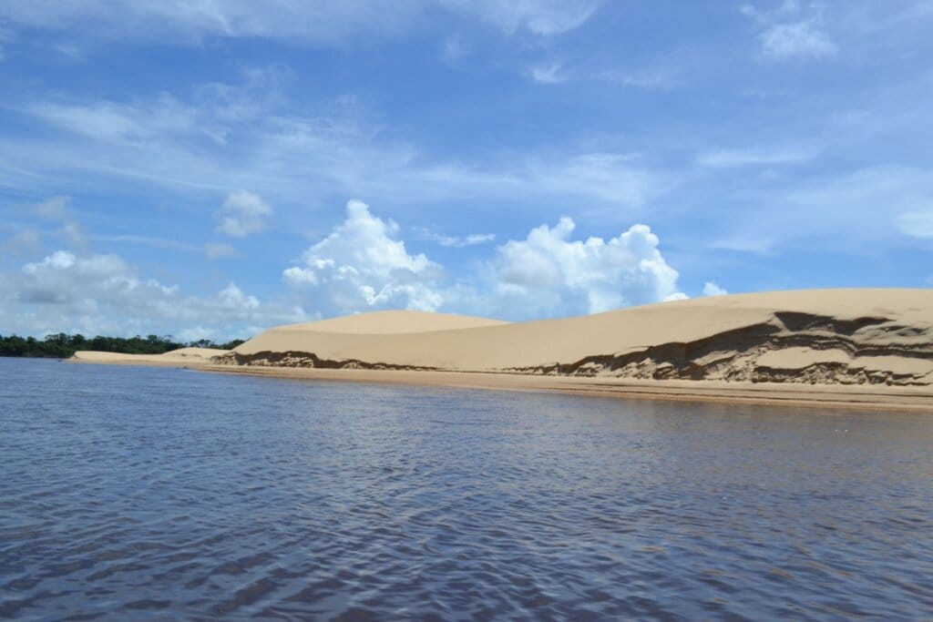 Vista das margens do Rio Preguiça com uma colina de areia e céu azul