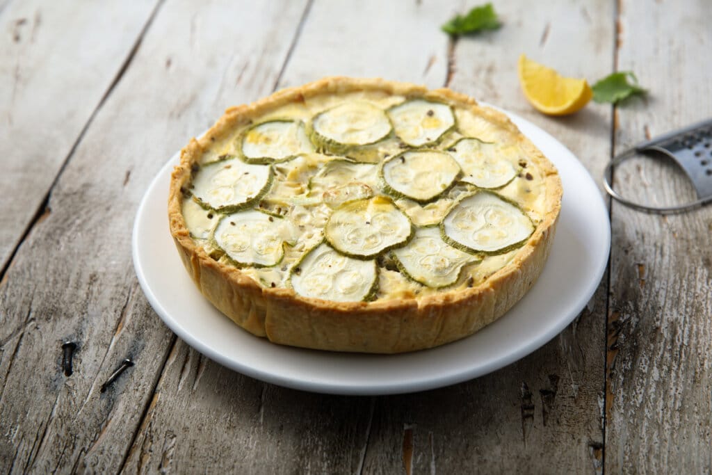Torta de abobrinha com castanha-de-caju em prato branco em cima de mesa de madeira