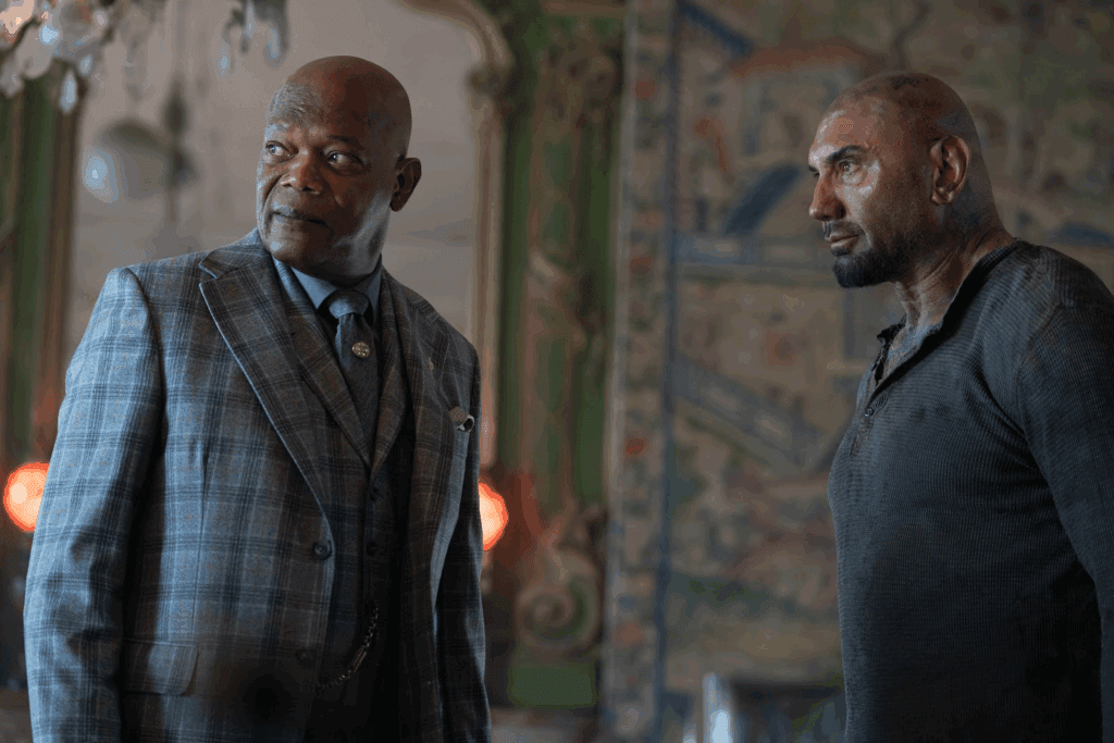 Imagem de dois homens carecas, um deles está usando roupas sociais xadrez e o outro casaco cinza escuro, ambos olhando para o mesmo lado