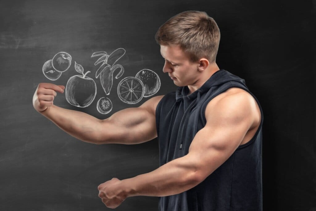 Homem usando regata preta e mostrando o músculo dos braços com um desenho de alimentos em giz