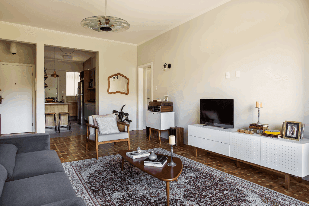 Sala de estar com móvel em branco com TV e cadeira de madeira com estofado branco e sofá preto e tapete estampado no chão 