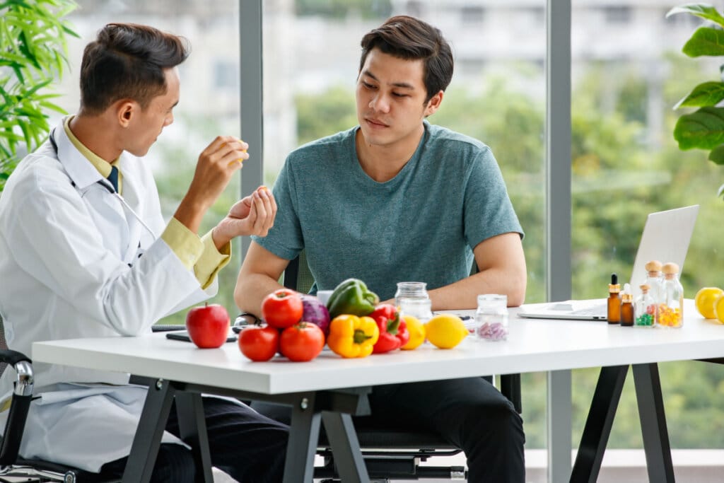 nutricionista e homem sentados conversando. A frente uma mesa com alimentos 