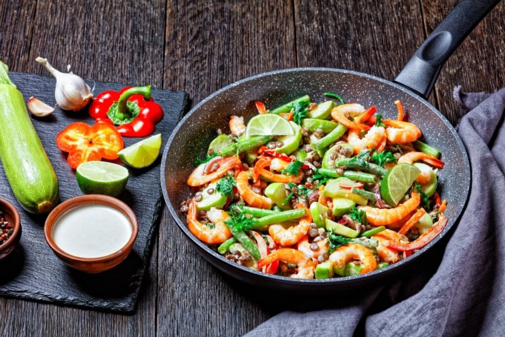 Salada mediterrânea morna de camarão com lentilhas, vagem, abobrinha, pimentão, couve e limão, servida em frigideira