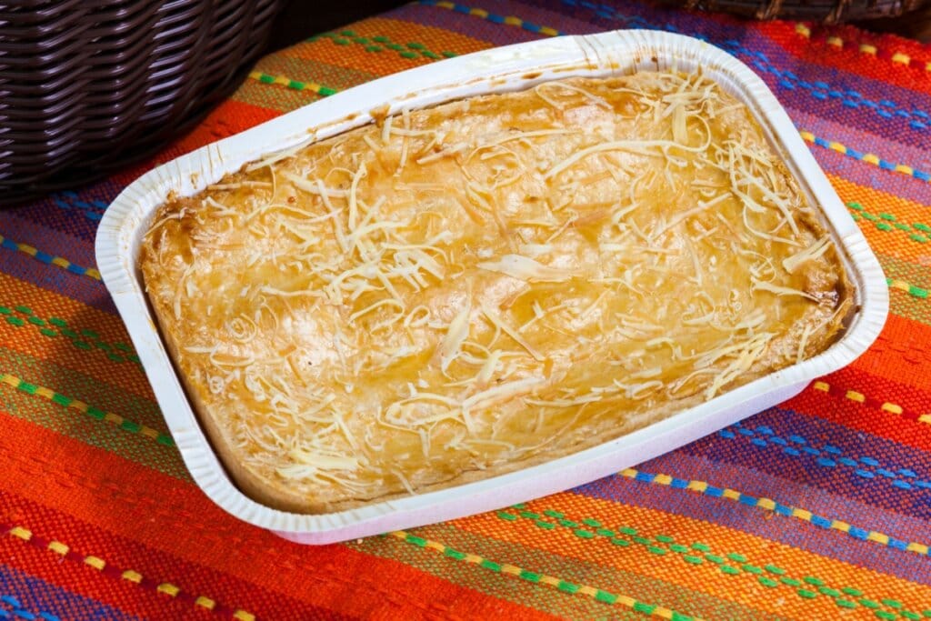 Torta de frango em uma forma de plástico branca polvilhada com queijo parmesão ralado