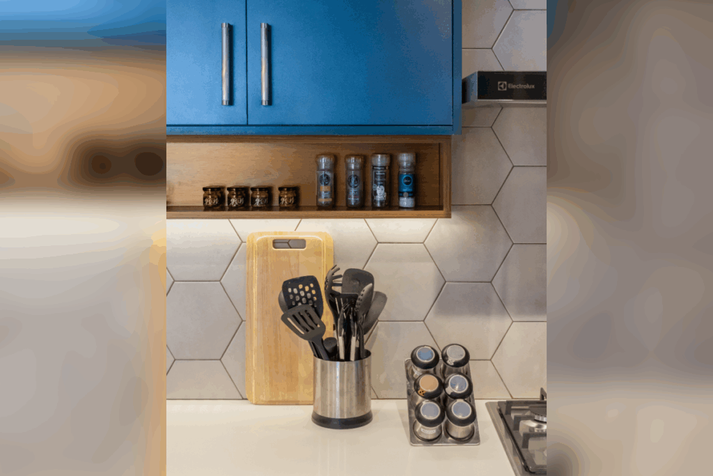 Detalhe de bancada de cozinha com suporte de inox para utensílios, tábua de corte, especiarias organizadas em prateleira embutida e armário azul superior