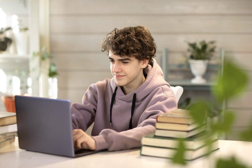 Jovem com o cabelo curto e usando blusa de moletom em roxo-claro estudando no notebook