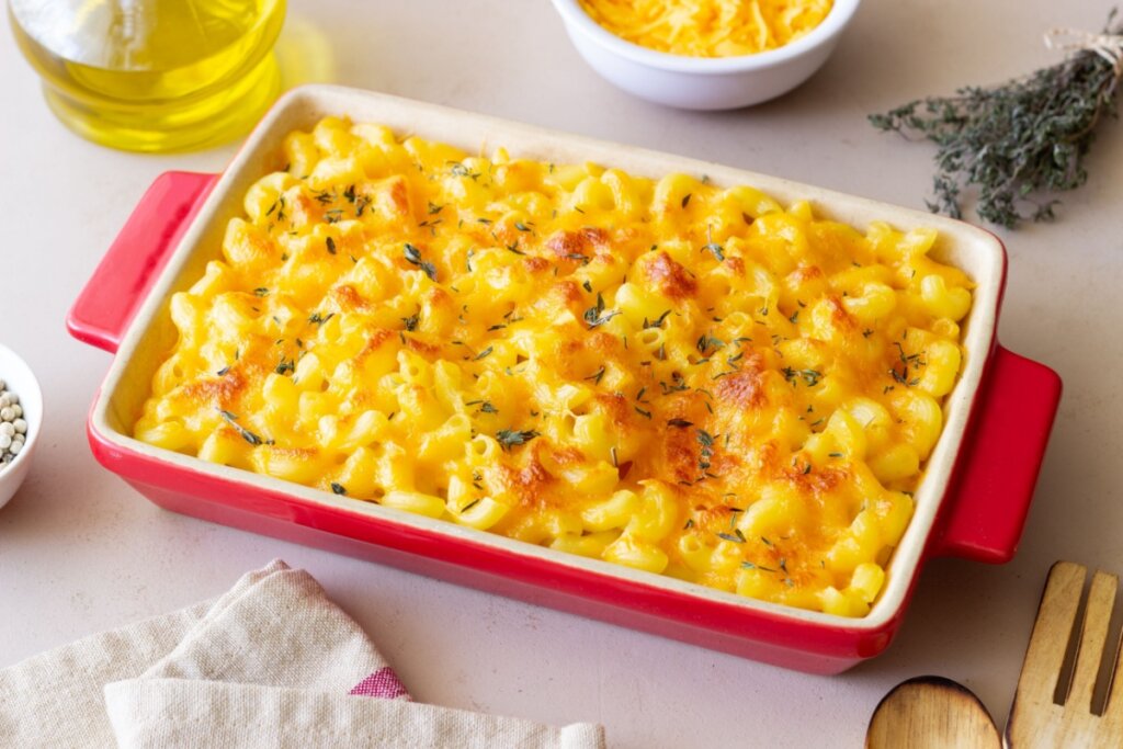 Mac and cheese servido em refratário de cerâmica branco e vermelho em cima de mesa com toalha branca