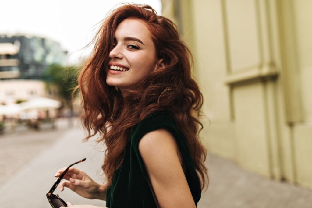 mulher de camiseta preta, de lado, com cabelo longo, ondulado e vermelho