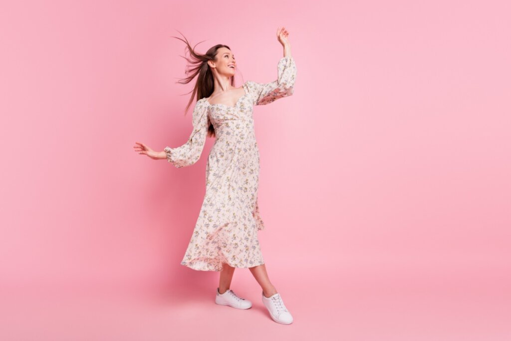 Mulher de vestido longo florido, cabelo sol e tênis branco em fundo rosa