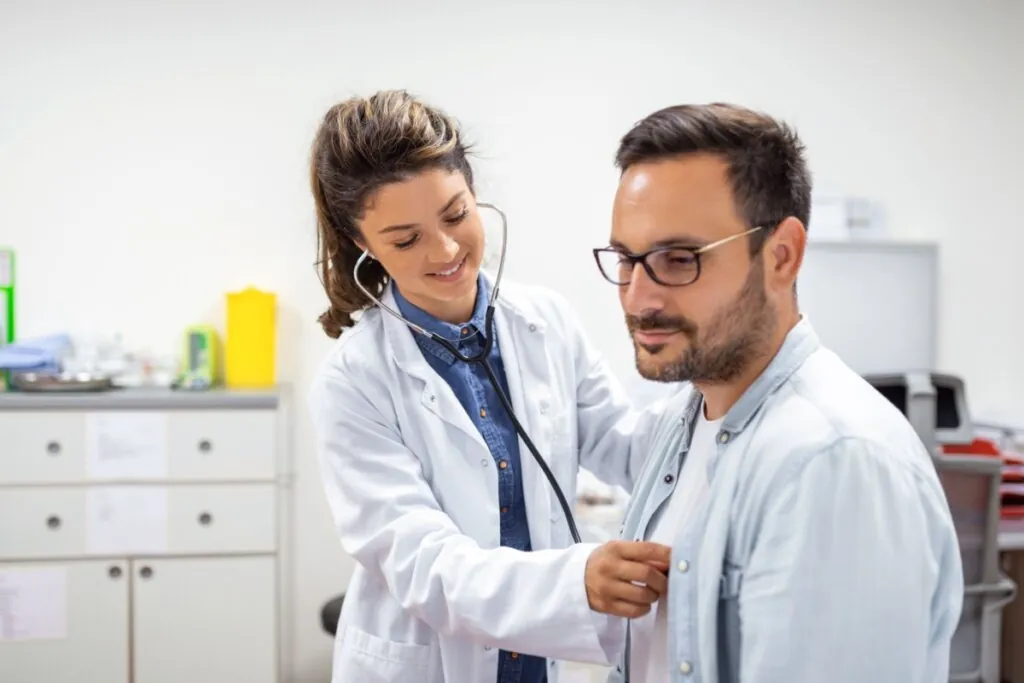 Médica examinando um homem com um estetoscópio em um consultório 