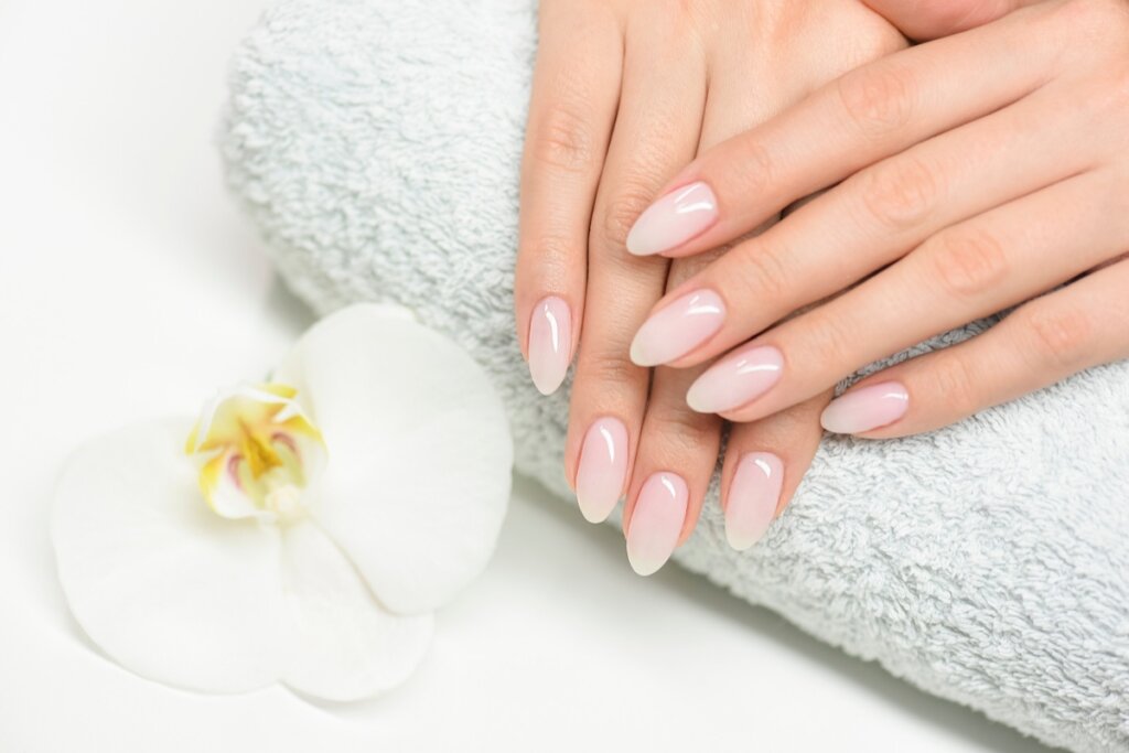 Unhas feminina pintadas no estilo Milk nails sobre uma toalha 