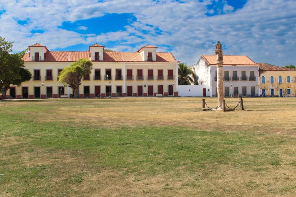 Campo de grama aberto com casa amarela e casa branca ao fundo 