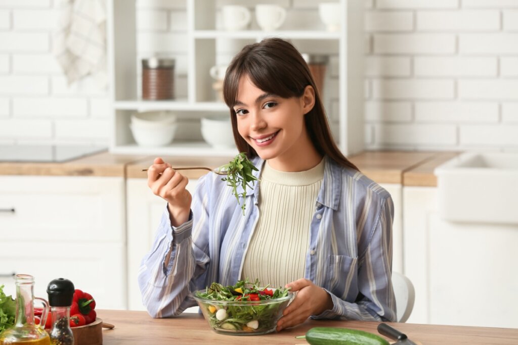 Mulher sentada em uma cozinha, comendo salada em um recipiente de vidro