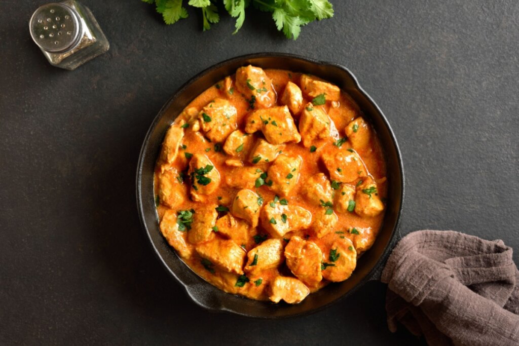 panela preta com pedaços de frango com molho alaranjado em superfície preta